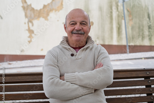 An elderly Spanish man is resting while sitting on a bench, enjoying a quiet moment outdoors 