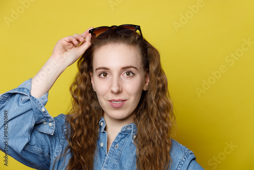 Young Woman Adjusting Sunglasses Against Yellow Background