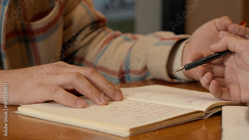 Hands making notes with a pen next to an open book on a cafe table