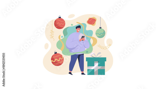 Happy man shops online on his phone near festive Christmas ornaments and a wrapped present