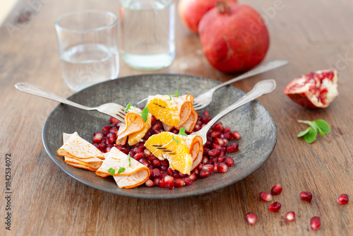Plate with pomegranate seeds, cured meats, and an orange.
