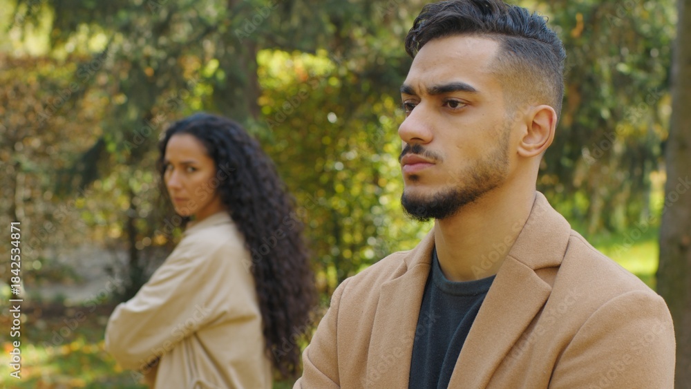 Fototapeta premium Frustrated Hispanic man offended angry separating from upset Arabian woman couple conflict in autumn park date sad boyfriend husband with girlfriend wife outdoors family quarrel ignoring each other
