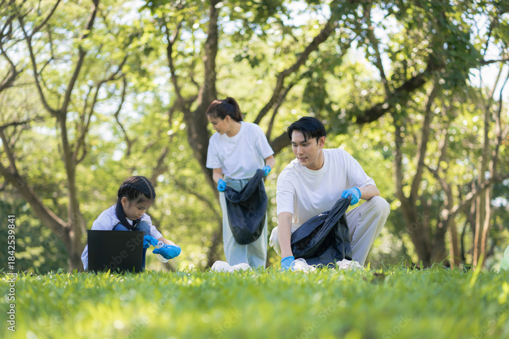 Fototapeta premium Asian family collects plastic bottles into black bags at a park on the weekend, Sustainable development and innovation green business concept.