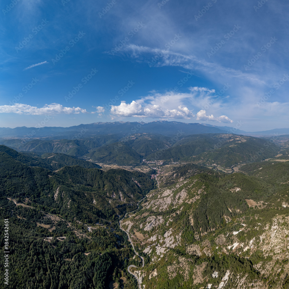 Obraz premium Expansive mountain valley with a winding road and distant snow-capped peaks under a blue sky