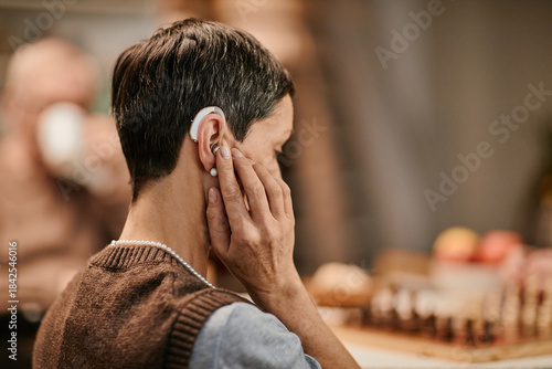 Foto Senior Caucasian woman adjusting hearing aid while sitting in nursing home, shor