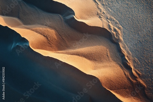Aerial view of sunlit sand dunes with deep blue shadows