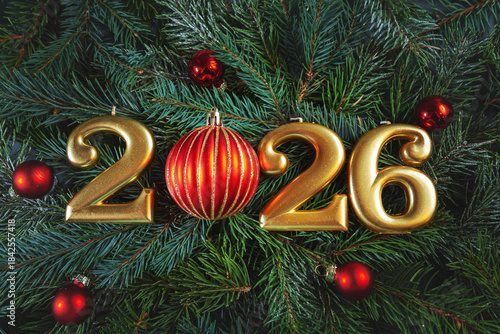 Golden numbers 2026 and Christmas balls against a background of fir branches.