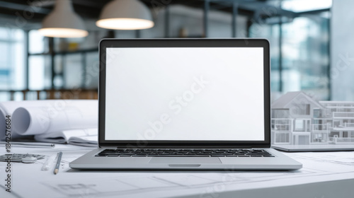 Architectural design on laptop screen with blueprints and model house on desk. Modern architect's workspace featuring a laptop displaying blank screen, rolled blueprints, and a miniature house model.