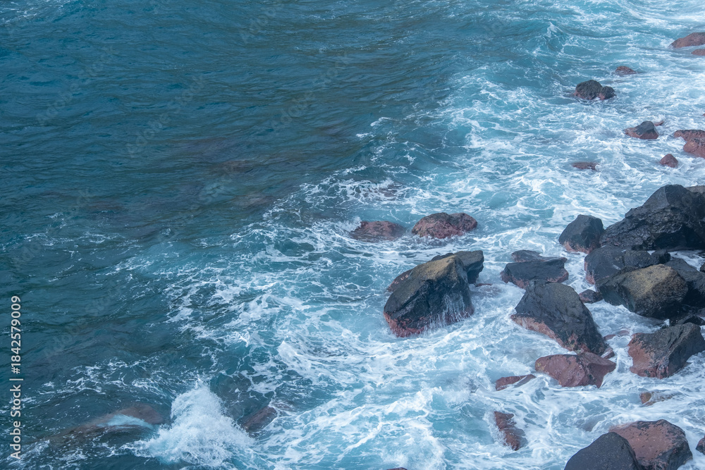 Naklejka premium Black Volcanic sand beach and blue water ocean in Madeira, coast Portugal, Atlantic waves sparkle in sun, warm Gulf Stream water flows, peaceful energy, marine life