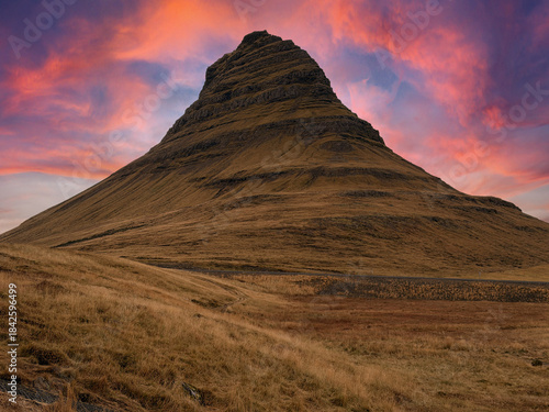 Kirkjufell mountain under a vibrant sunset sky painted in orange, red, and pink hues, creating a dramatic and colorful Icelandic landscape.