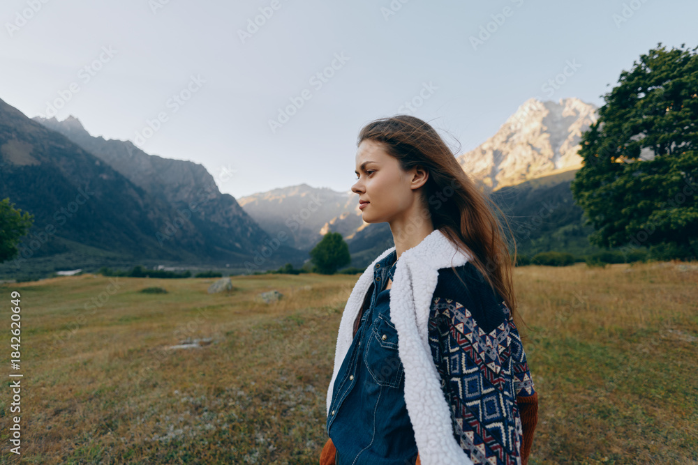 Fototapeta premium woman portrait mountains meadow landscape nature profile outdoors young female traveler in patterned jacket standing in alpine valley, contemplative and peaceful expression with distant peaks and