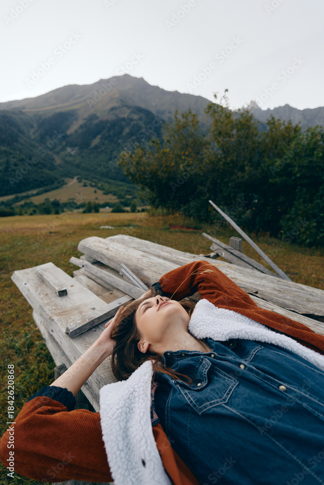 Fototapeta premium Woman lying on a wooden picnic table in mountain nature outdoors, relaxation and landscape scene with meadow and trees, portrait of calm travel and peaceful escape feeling.