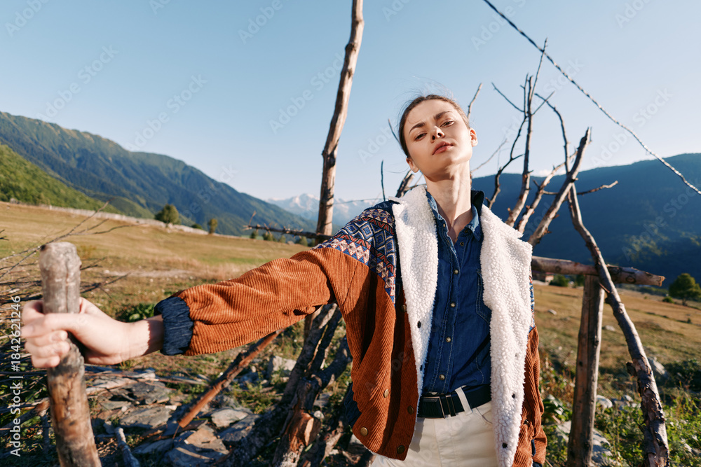 Fototapeta premium woman portrait in countryside mountains, fashion model leaning on wooden fence, rural lifestyle and outdoor clothing with relaxed expression and scenic natural landscape backdrop