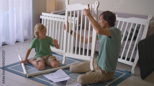 Father and son assembling a baby crib together for their soon arriving son and brother. Family teamwork, bonding, parenting support and preparation for newborn concept.