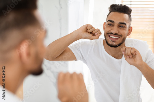 Fotografie A young man brushes his teeth and flosses in a bright bathroom