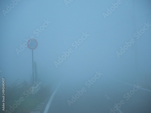 朝の濃霧の天気の中の道路と速度制限の印の様子