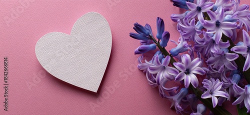 White heart cutout beside vibrant purple hyacinth flowers on a pink background