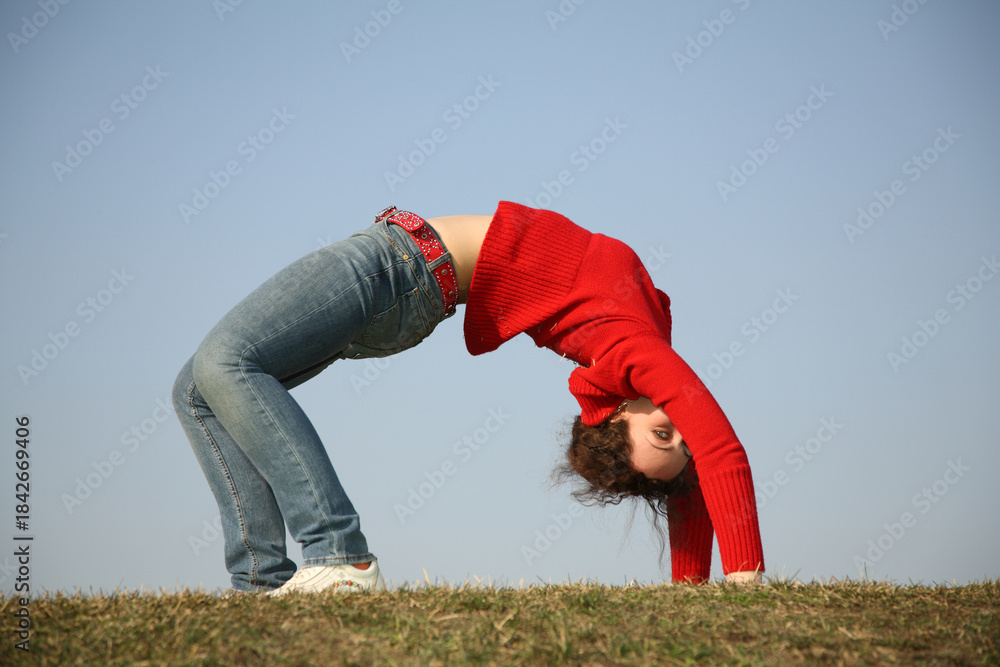 Naklejka premium A woman is doing a handstand on a grassy field. Concept of freedom and strength, as the woman is able to balance herself in a challenging position