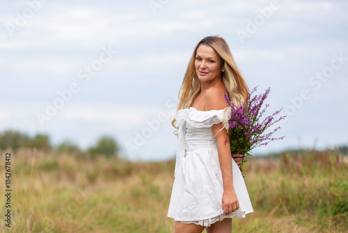 Young woman in white dress holding flowers in a green field on a cloudy day