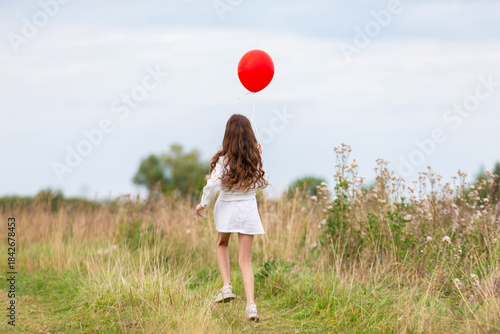 Girl walking on a path in nature holding a red balloon during a cloudy day
