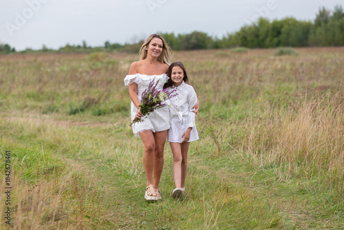 Mother and daughter walk together in a field holding flowers during a serene afternoon