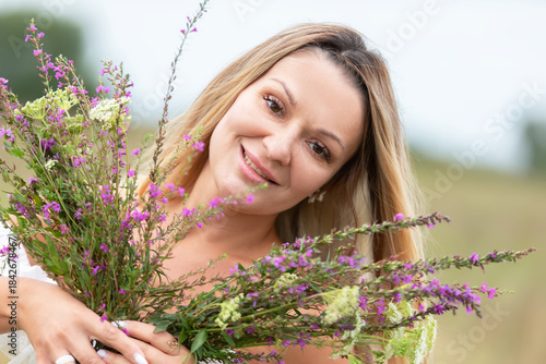 Smiling woman holding wildflowers in a sunny meadow during a warm afternoon