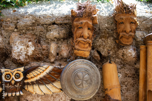 Wooden masks and carvings displayed on a rustic stone wall in a vibrant artisan market during the afternoon sunlight
