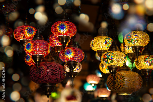Colorful decorative lanterns illuminate a marketplace filled with vibrant patterns and warm light during an evening setting