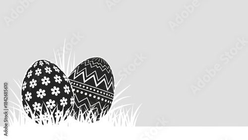 Two black and white decorated Easter eggs nestled in grass, with intricate patterns, on a light gray background.
