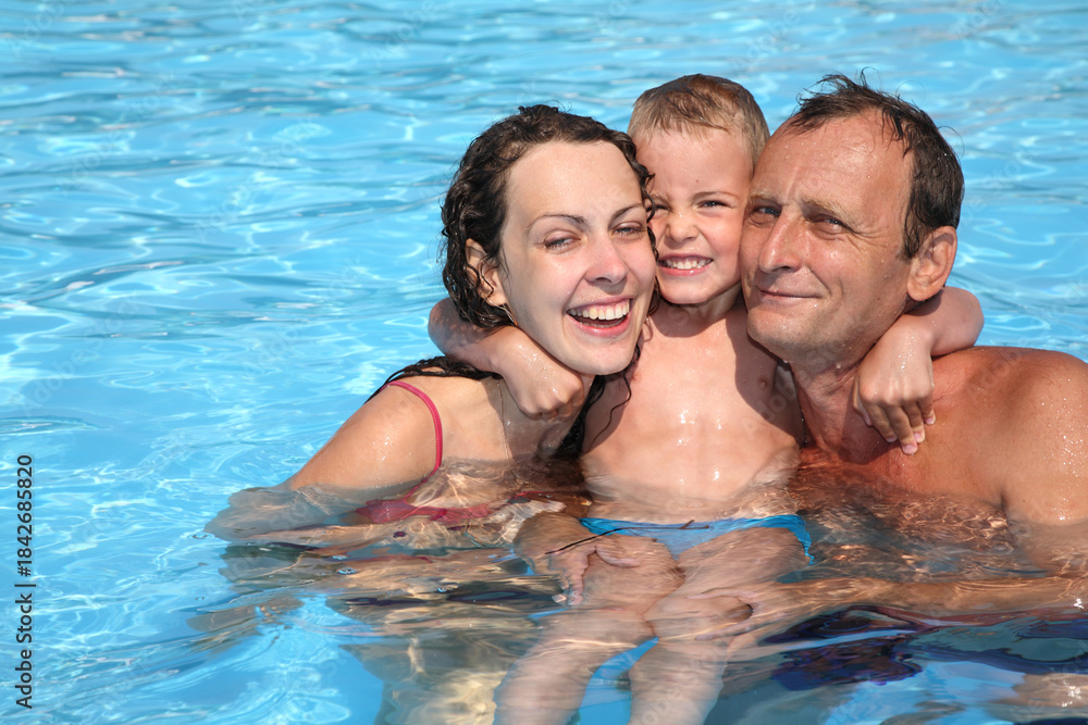 Fototapeta premium A family of three is in the water, with a woman and a child hugging a man. Scene is happy and joyful, as the family senior is enjoying their time together in the pool