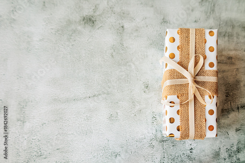 Wallpaper Mural Minimal gift box wrapped in white and gold polka dot paper with rustic ribbon, placed on modern textured background. Clean composition for creative branding, blogs, and promotions Torontodigital.ca