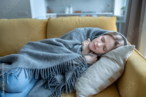 Exhausted woman lying on sofa shivering under blanket. Emotional fatigue, mental health problems, deep social isolation, depression. Sick unwell female with cold, flu symptom suffer chills, malaise.