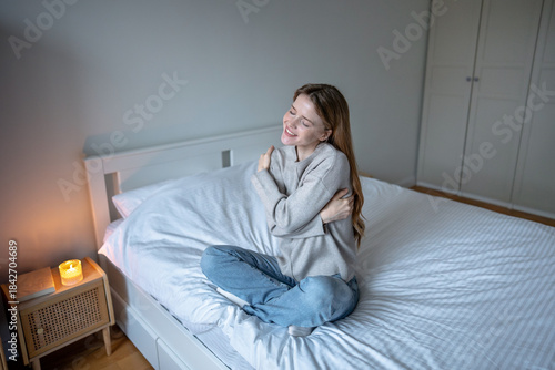 Foto Happy smiling woman sitting on bed gently hugging herself, practicing self-compassion