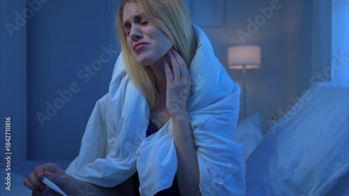 A young woman with a cold, checks her temperature, wraps herself in a blanket, and goes to sleep