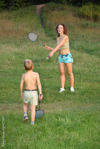 A young girl is playing tennis with a boy. The girl is wearing a blue and white striped shirt and blue shorts