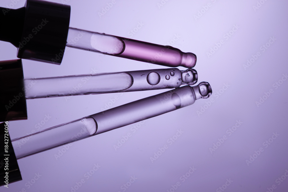 Fototapeta premium Three glass pipettes with facial serum on light purple background. Front view. Frontal close-up view of liquid gel/essential oil, banner for advertising anti-aging cosmetic product with bakuchiol, spi