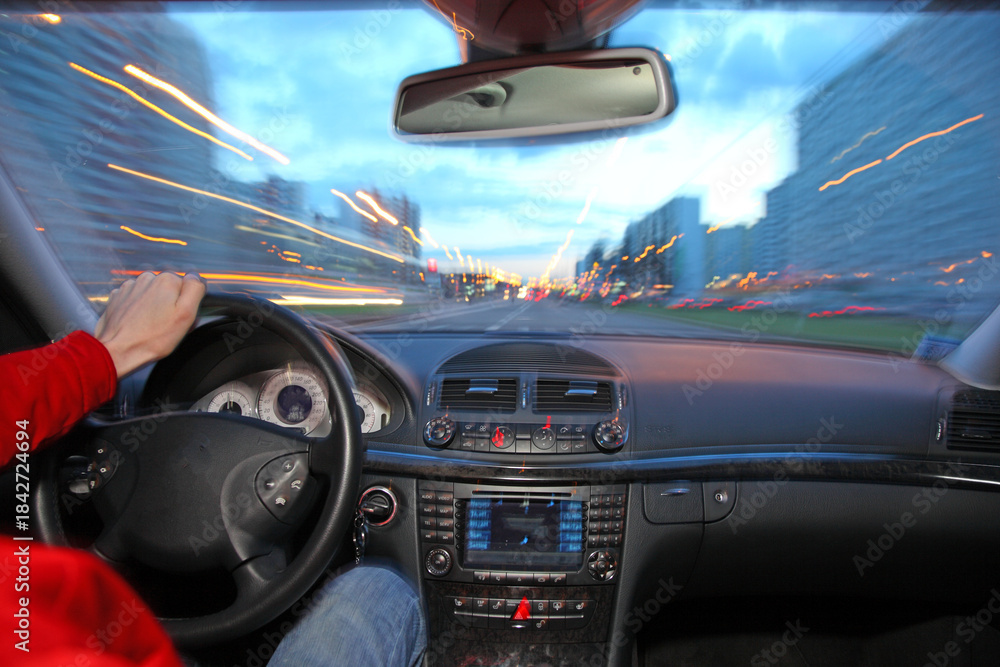 Fototapeta premium A person is driving a car with the windows down and the radio on. The car is moving quickly down a city street