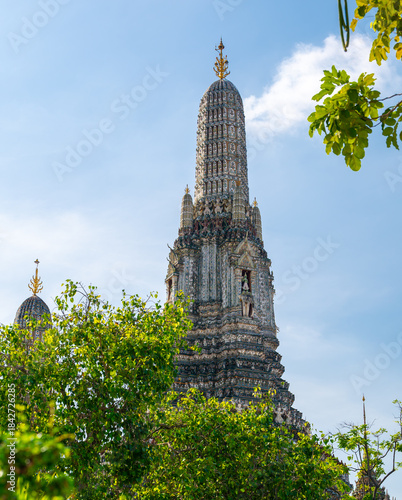 Detailed view of the ornate towers of Wat Arun in Bangkok, Thailand, showcasing rich ceramic floral patterns, sculpted figures, and intricate decorations under bright daylight.