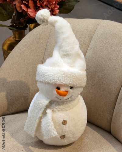 Vista de cerca de muñeco de nieve con sombrero de Santa Claus y bufanda de color blanco en una butaca 