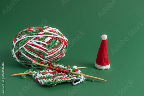 Christmas knitting wool and needles with Santa hat on green background with copy space