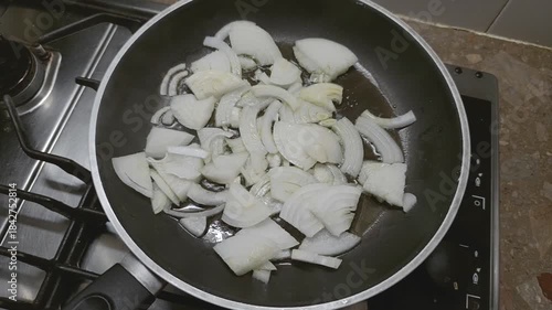 Sliced onions sizzle in hot oil, slowly turning soft, in the pan.
