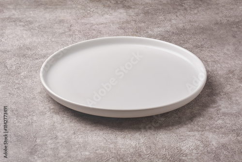 empty matte white ceramic plate with round rim on textured grey concrete stone background surface, rustic dining or menu concept with copy space