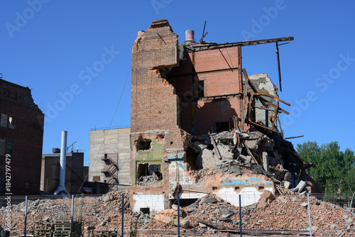 An abandoned factory with pipes, dilapidated brick buildings and pieces of walls under a clear blue sky