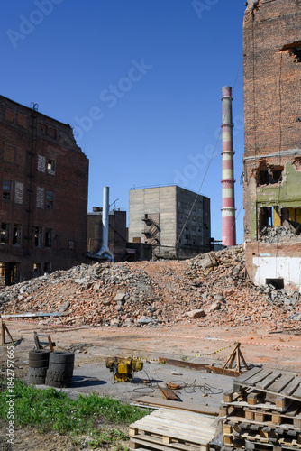 An abandoned factory with pipes, dilapidated brick buildings and pieces of walls under a clear blue sky