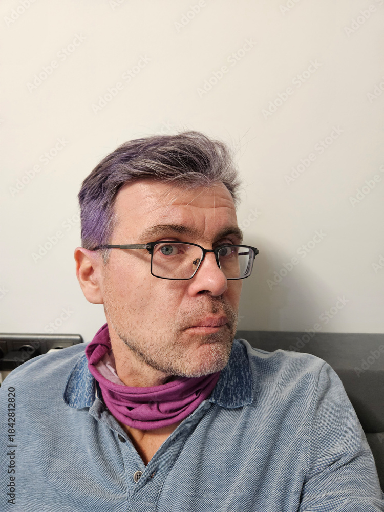 Fototapeta premium Man with purple hair and glasses. He is wearing a blue shirt and a purple scarf. He is looking at the camera
