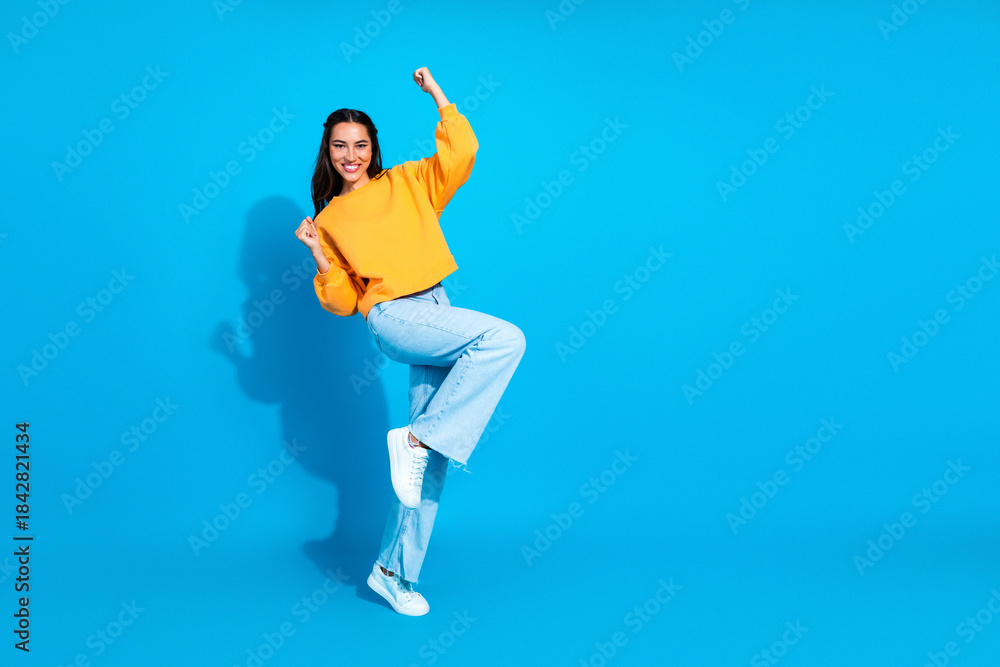 Obraz premium Young woman in yellow sweater dancing against blue background creating a fun stylish lifestyle and shopping vibe