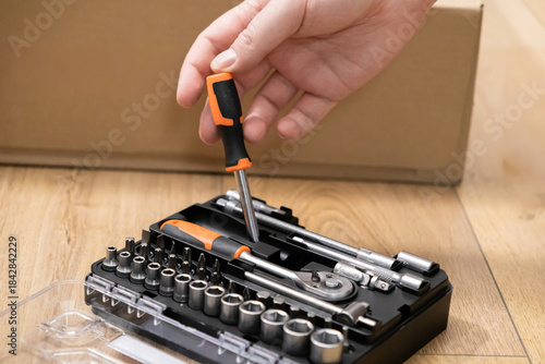 A hand precisely selects an orange-handled screwdriver from a complete comprehensive repair tool kit, perfect for efficient furniture assembly and home improvement tasks