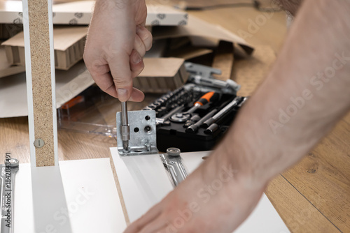 Wallpaper Mural Person's hands carefully screwing a metal hinge onto a white flat-pack furniture panel, illustrating home assembly, DIY projects, and personal effort Torontodigital.ca