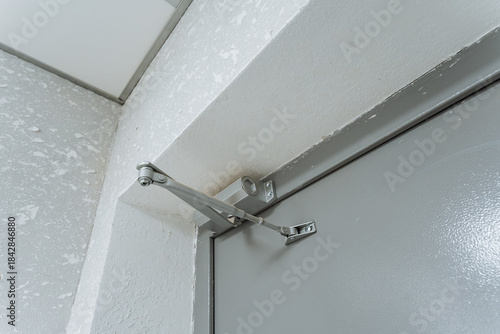 door hardware components, metal door closer with adjustable arm, entryway door mechanism featuring bolts and hinge details, adjustable arm door closer mounted on metallic frame with hardware details