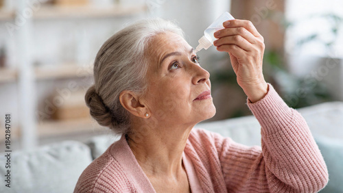 Elderly woman applying eye drops while sitting on a sofa indoors  